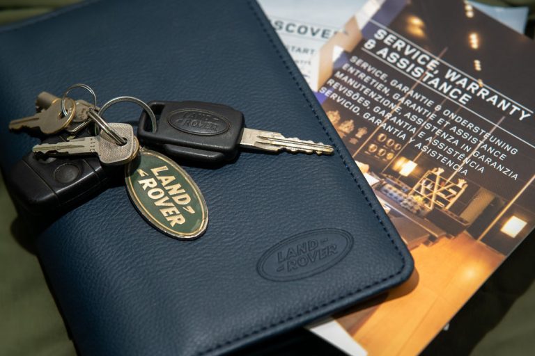Log book of a vehcile with a key on top. There is also a Landrover badge on the keychain